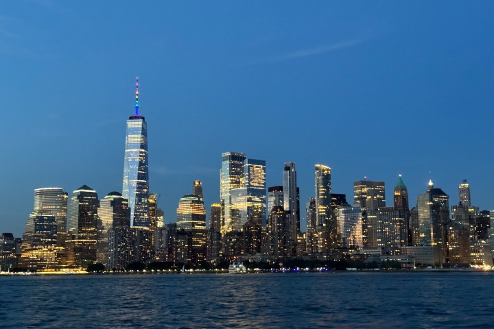 City skyline at dusk with illuminated skyscrapers reflected on water.