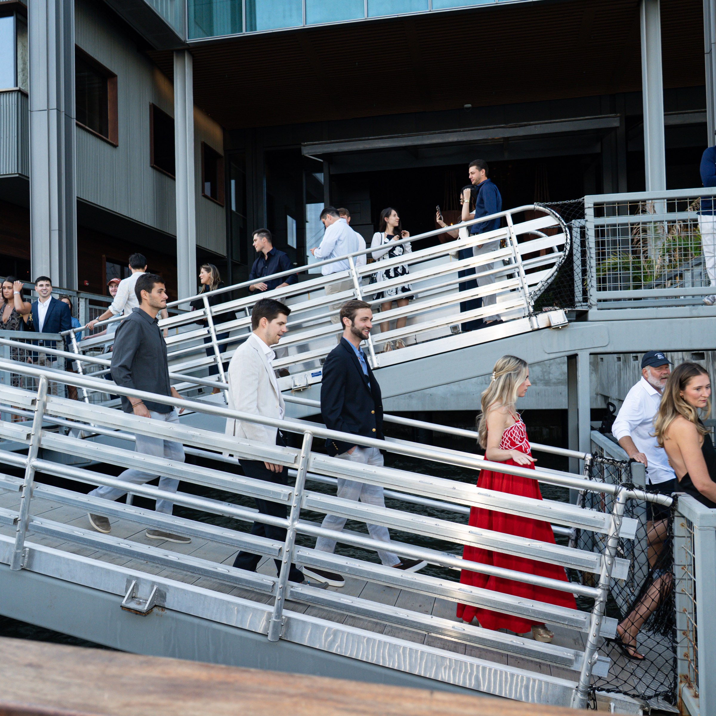 People in formal wear walking down a ramp at a modern building exterior.