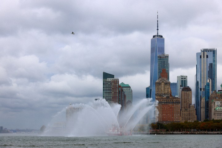 City skyline with skyscrapers and a boat spraying water into the air.