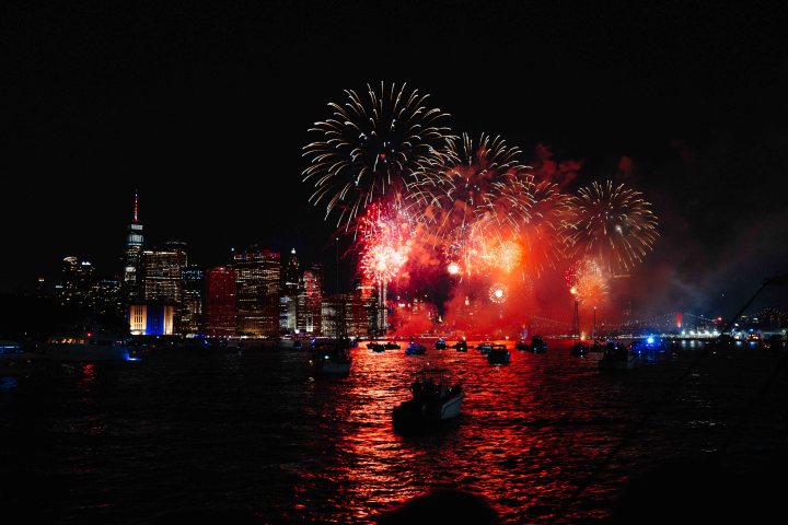 Fireworks over a city skyline at night with boats on the water.