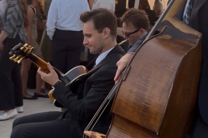 Musicians playing guitar and double bass on a boat during sunset with people mingling in the background.