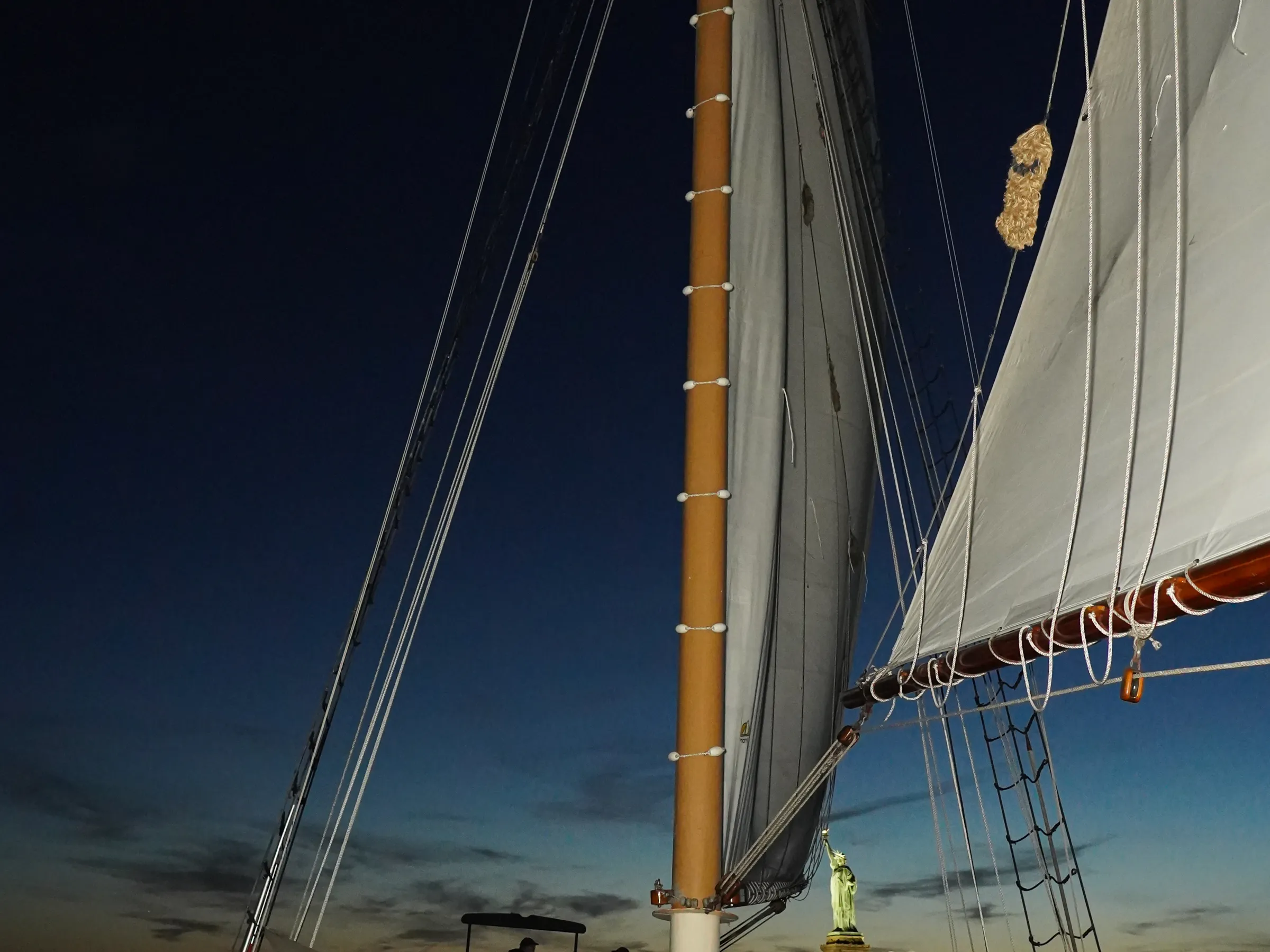 People on a sailboat at dusk with Statue of Liberty visible in the background.