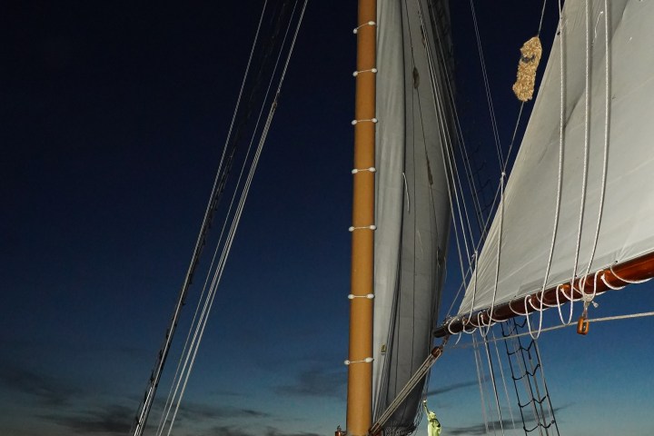 People on a sailboat at dusk with Statue of Liberty visible in the background.