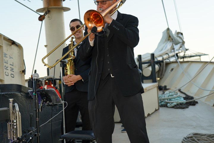 Musicians playing trombone and saxophone on a ship deck.