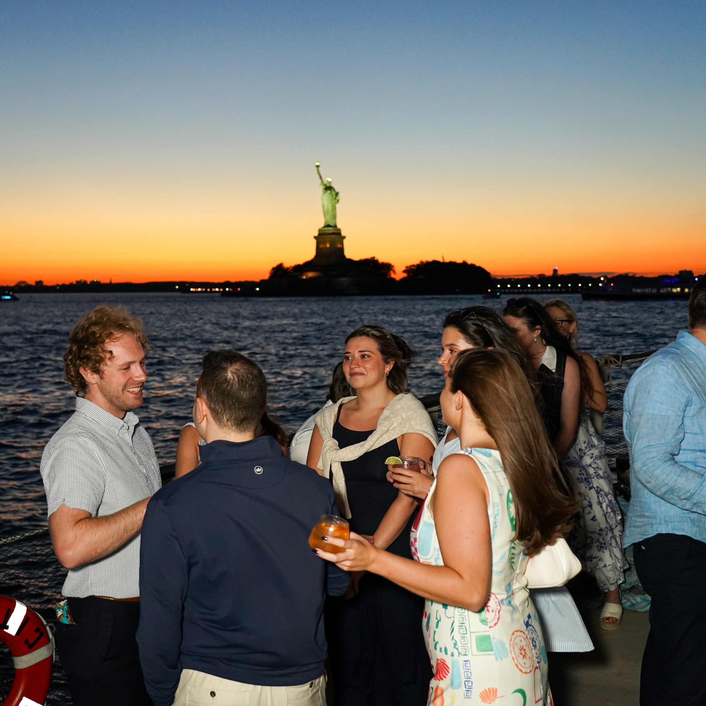 Group of people socializing at sunset near the Statue of Liberty.