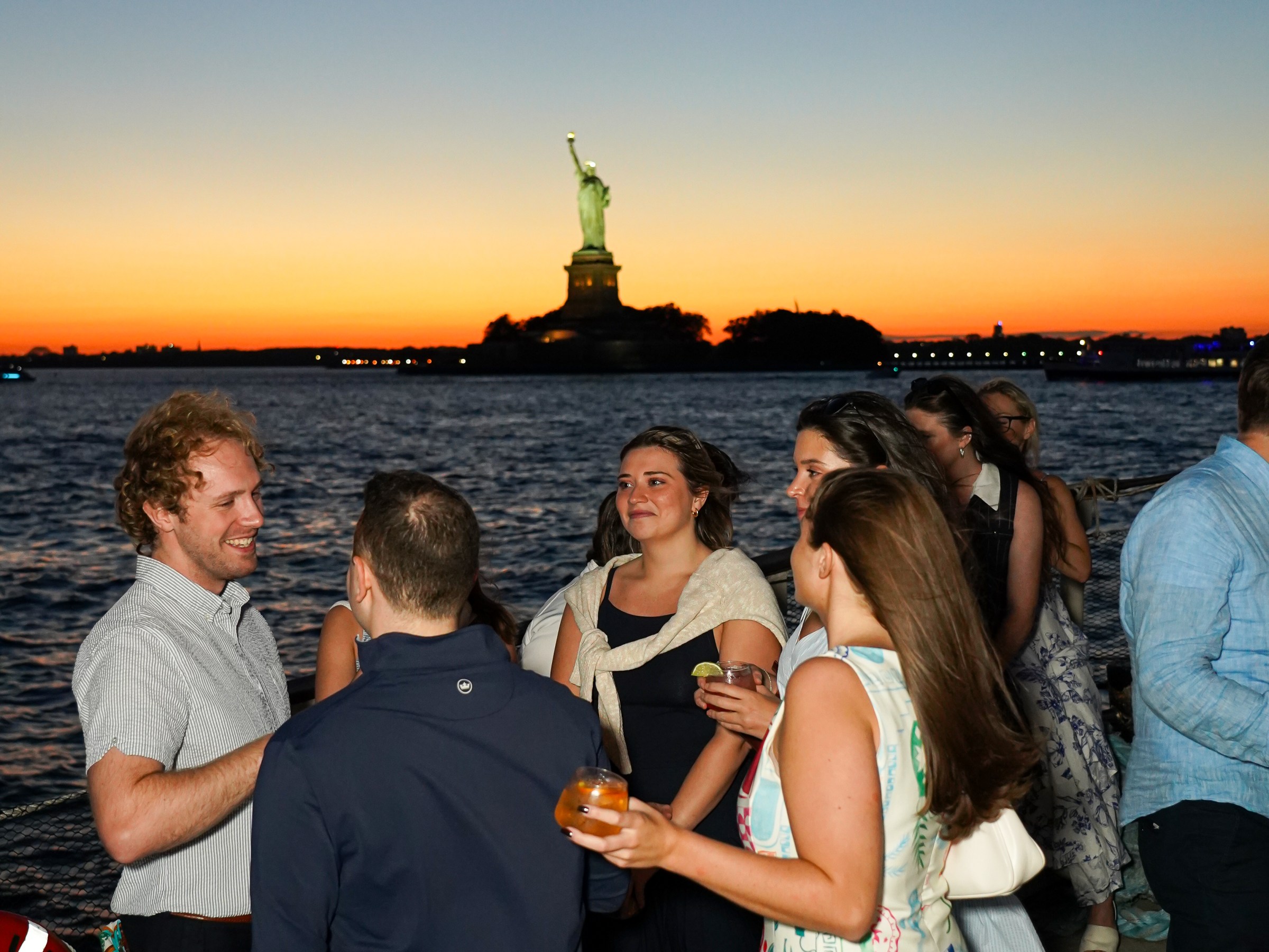 Group of people socializing at sunset near the Statue of Liberty.