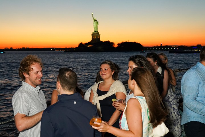 Group of people socializing at sunset near the Statue of Liberty.