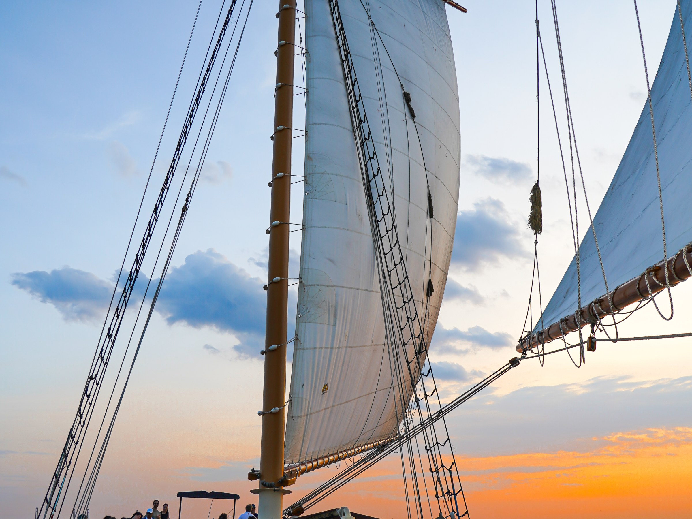 People sailing on a boat with large sails at sunset, socializing and enjoying the view.