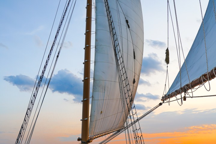 People sailing on a boat with large sails at sunset, socializing and enjoying the view.