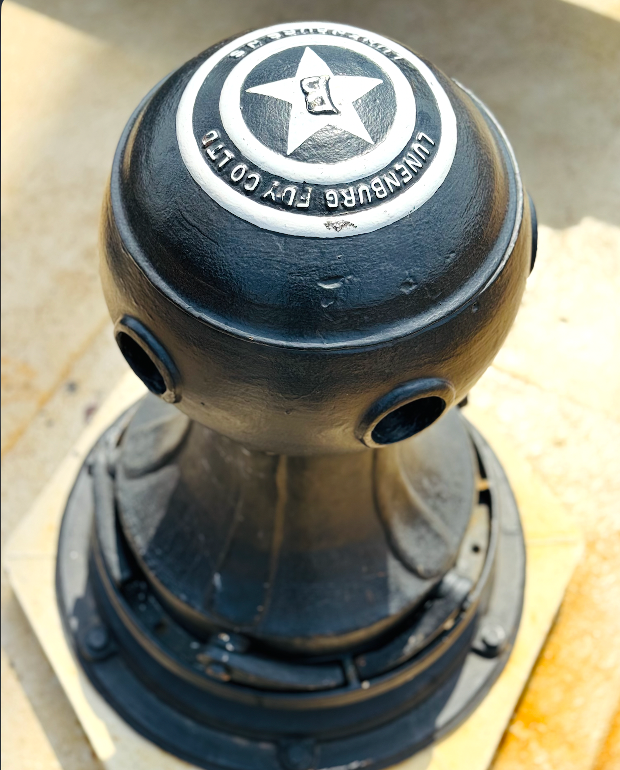 Black metal bollard with star emblem and text on top, taken from above on concrete.
