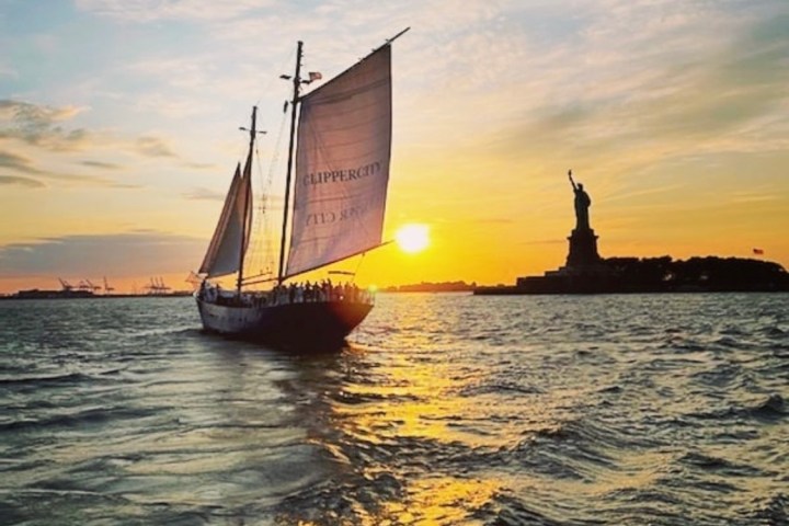 Sailboat on water at sunset near a statue silhouette.
