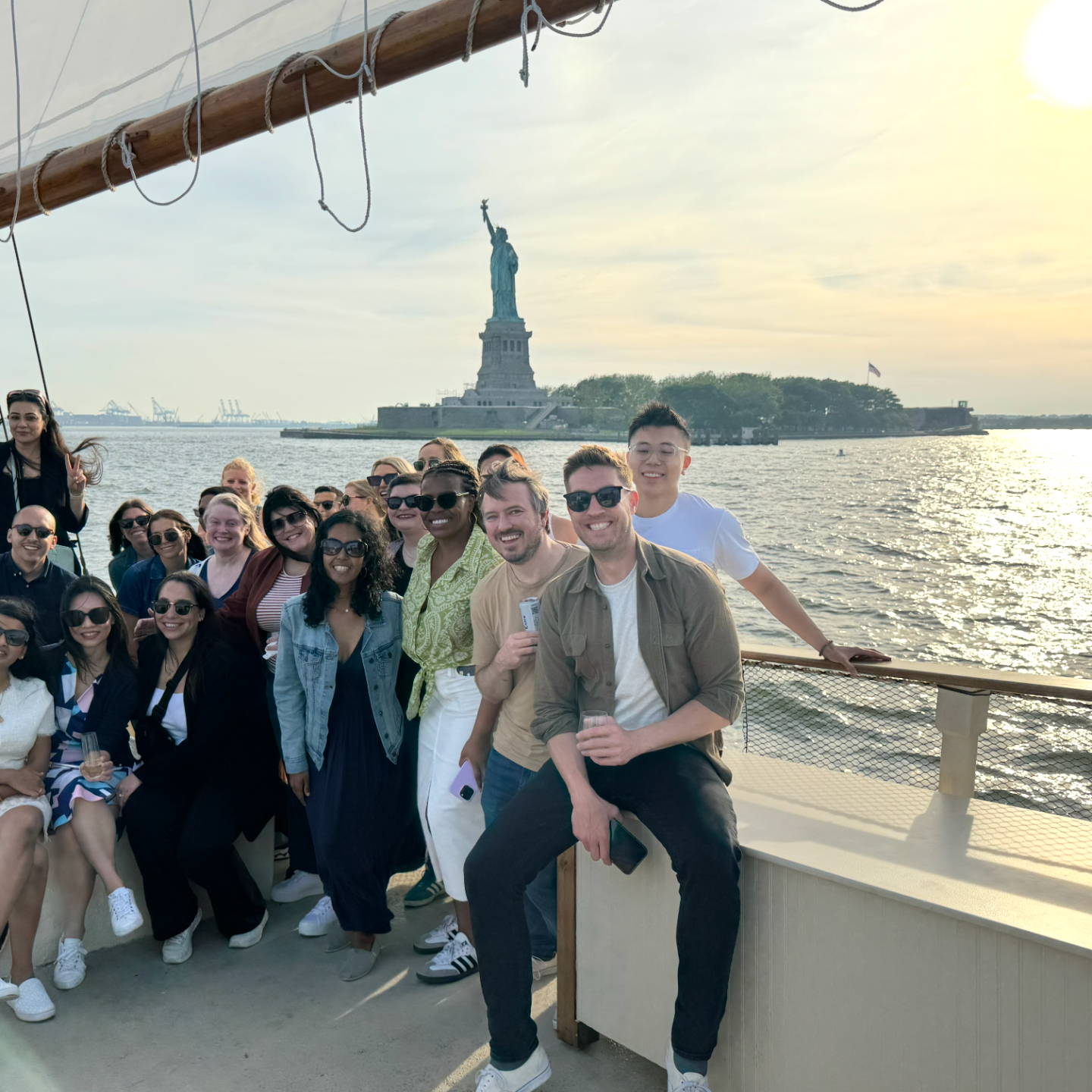 Group of people on a boat with the Statue of Liberty in the background during sunset.