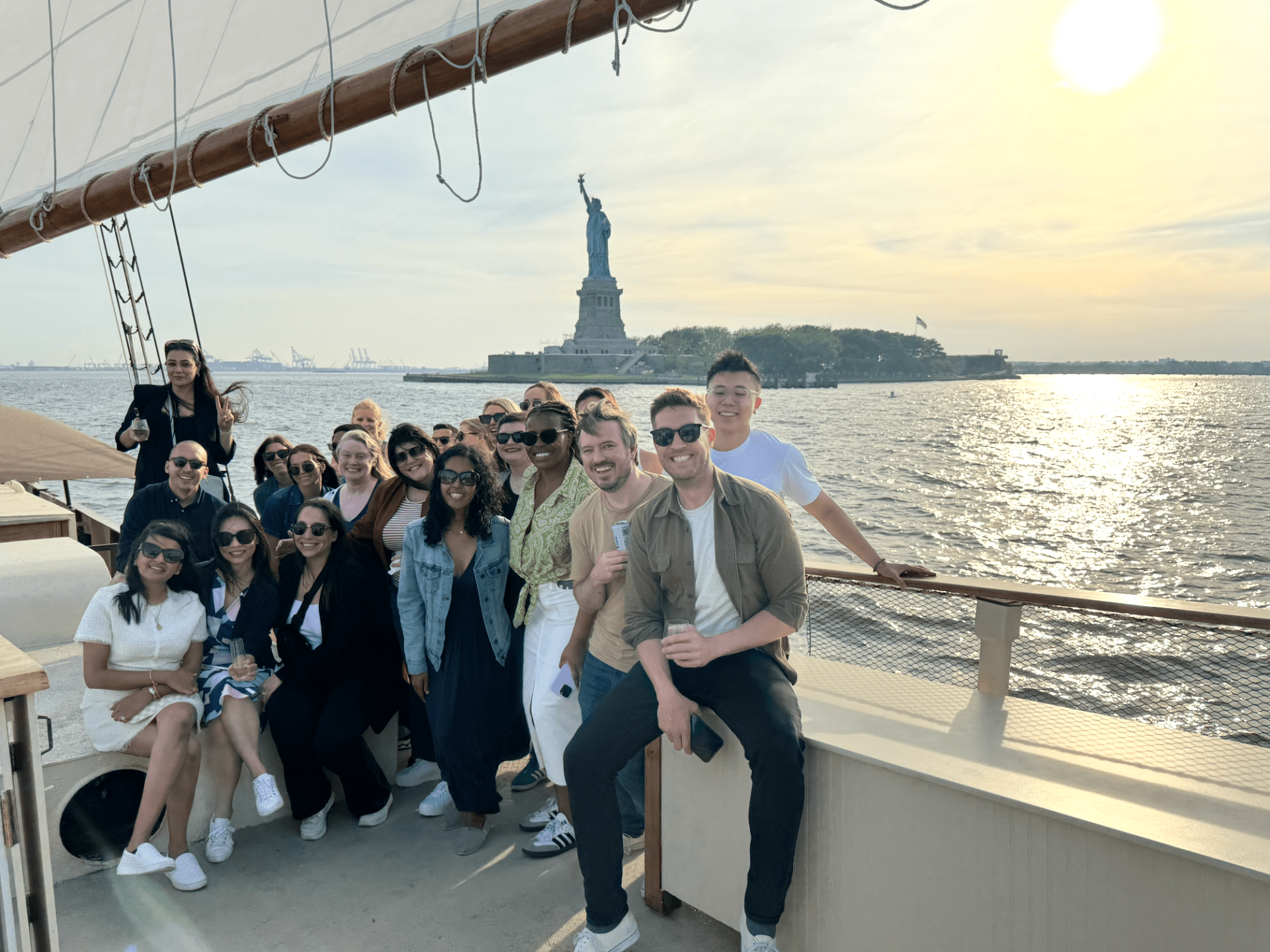 Group of people on a boat with the Statue of Liberty in the background during sunset.