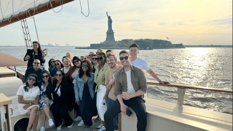 Group of people on a boat with the Statue of Liberty in the background during sunset.