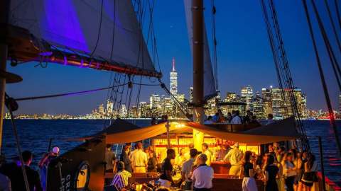 People socializing on a sailboat at night with city skyline in the background.