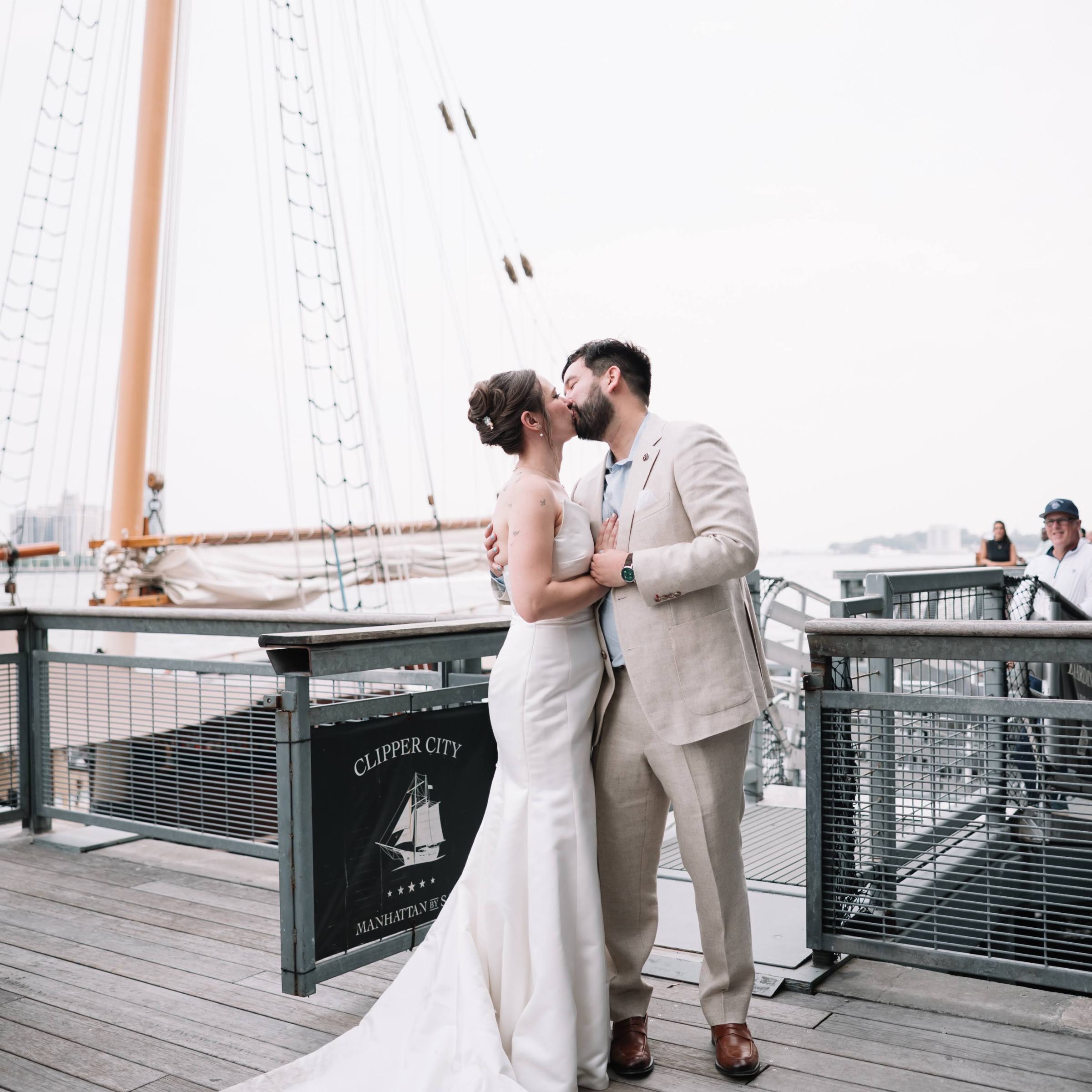 Bride and groom kissing on a ship deck with a tall mast in the background.