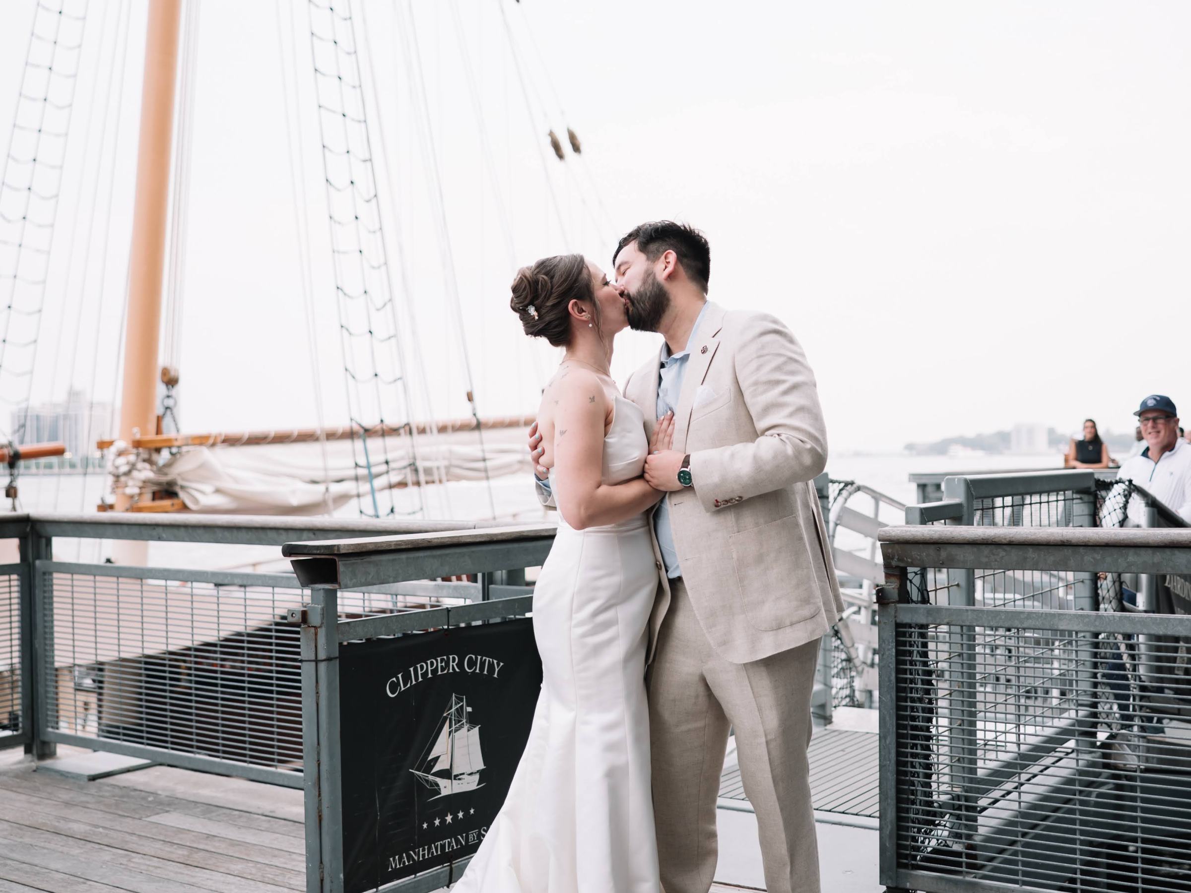 Bride and groom kissing on a ship deck with a tall mast in the background.