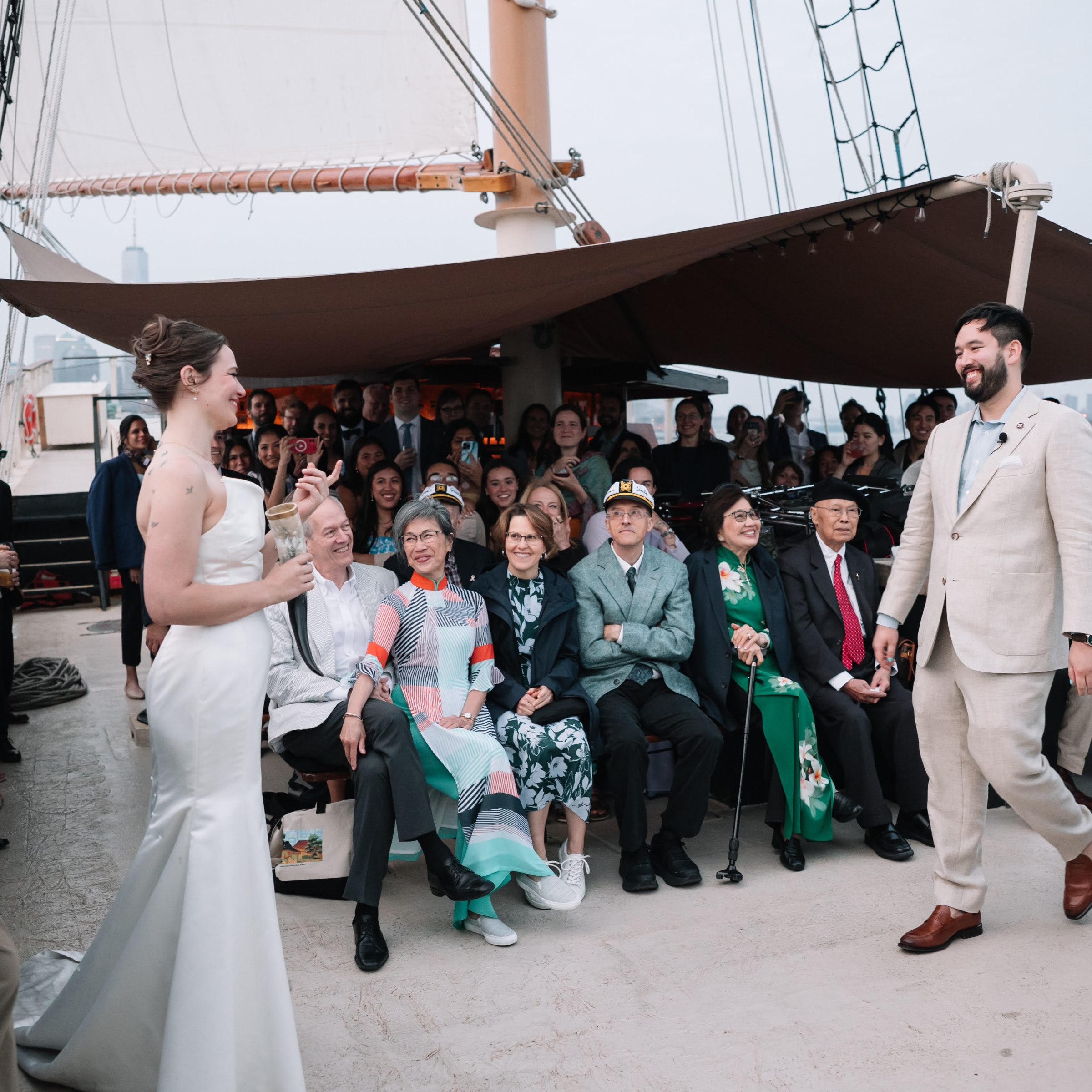 Bride and groom smiling on a boat with guests seated and standing around them.