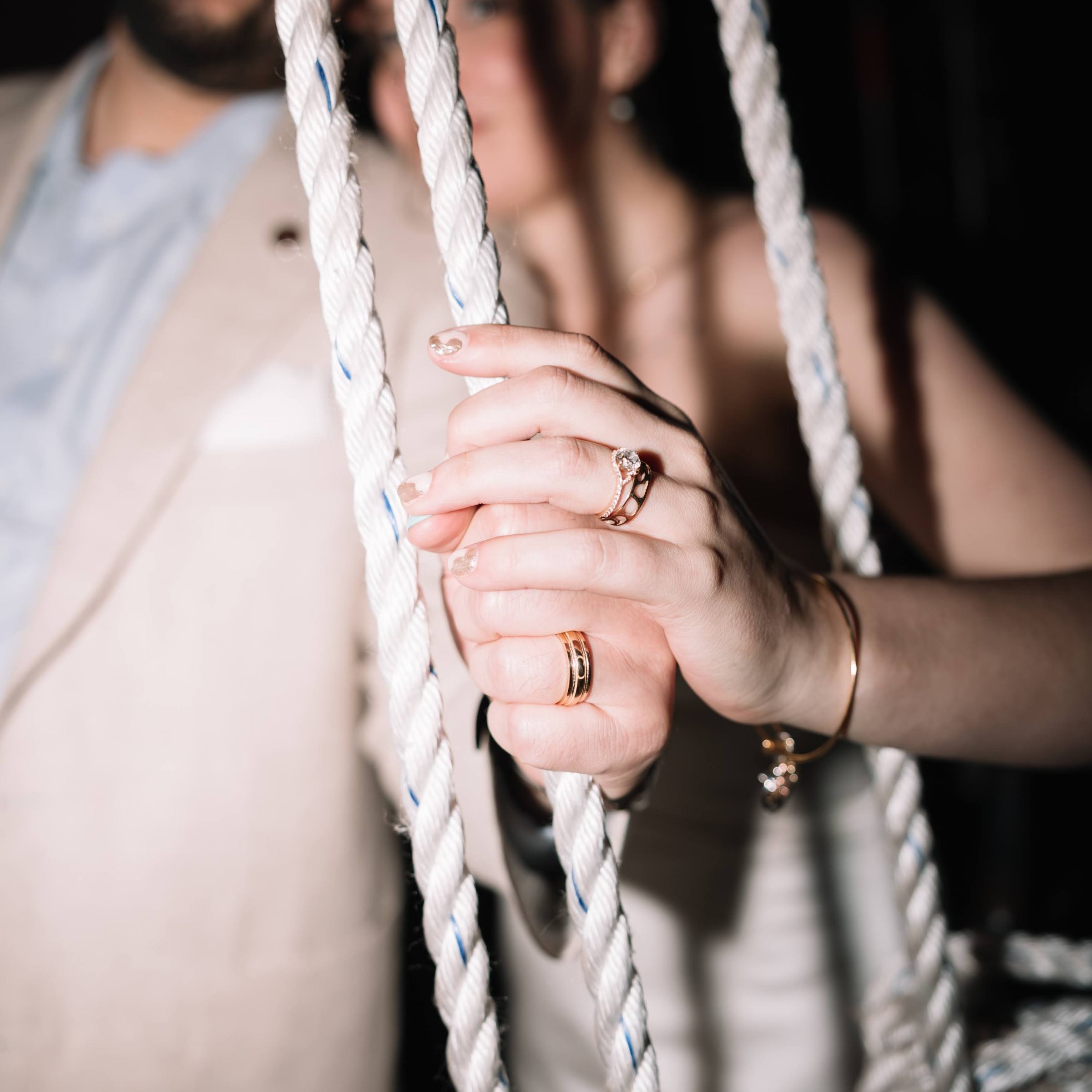 A close-up of a woman's hand with rings holding a rope, blurry people in the background.