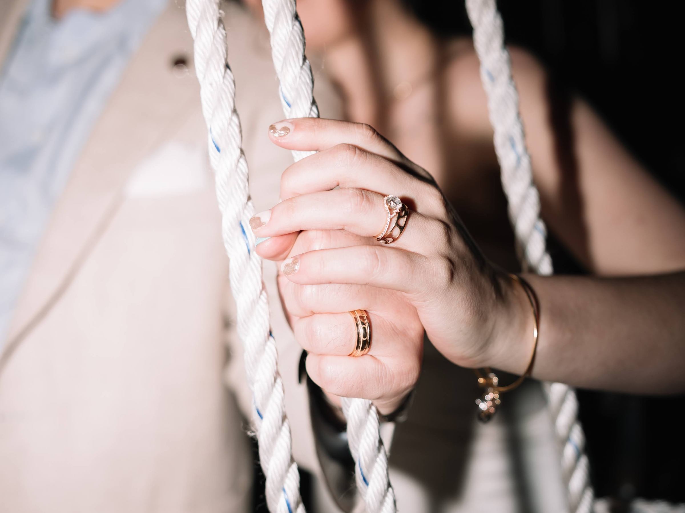 A close-up of a woman's hand with rings holding a rope, blurry people in the background.