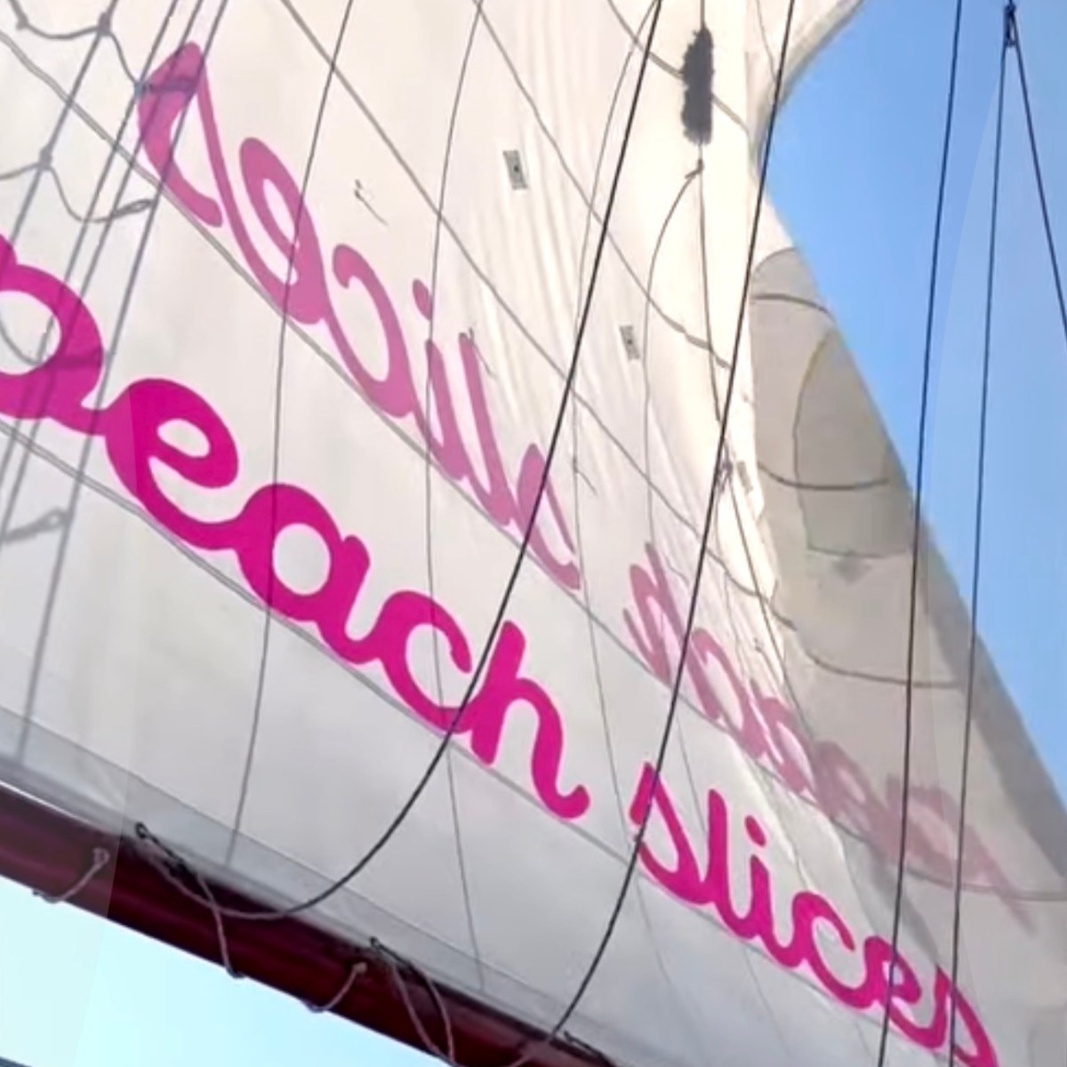 White sail with pink text 'peach slices' on a clear day with blue sky.