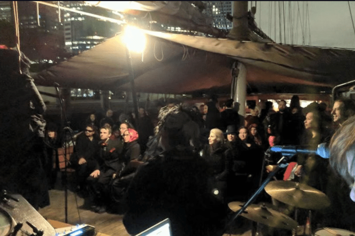 People gathered under a tent on a ship deck at night with a drummer visible.