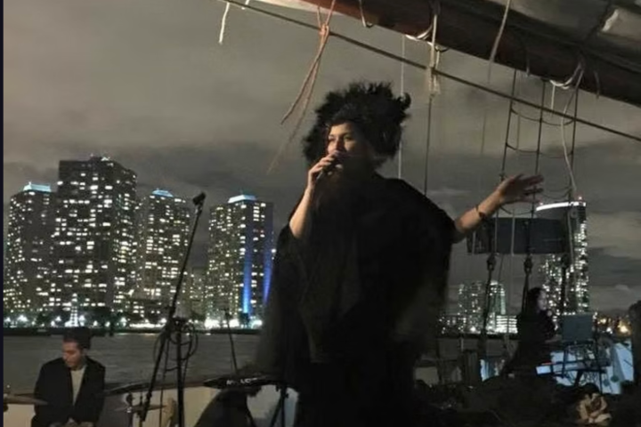 Singer performs on a dimly lit stage with city skyscrapers in the night background.