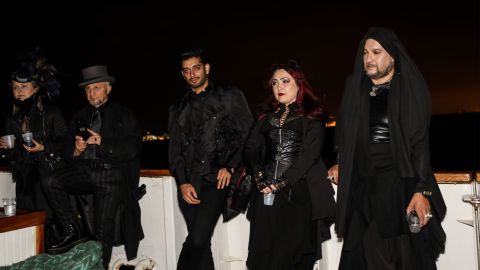 Five people dressed in black gothic attire on a boat at night.