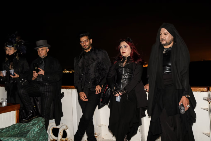 Five people dressed in black gothic attire on a boat at night.
