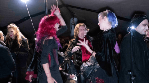 People in colorful outfits dancing and chatting at a lively indoor event.